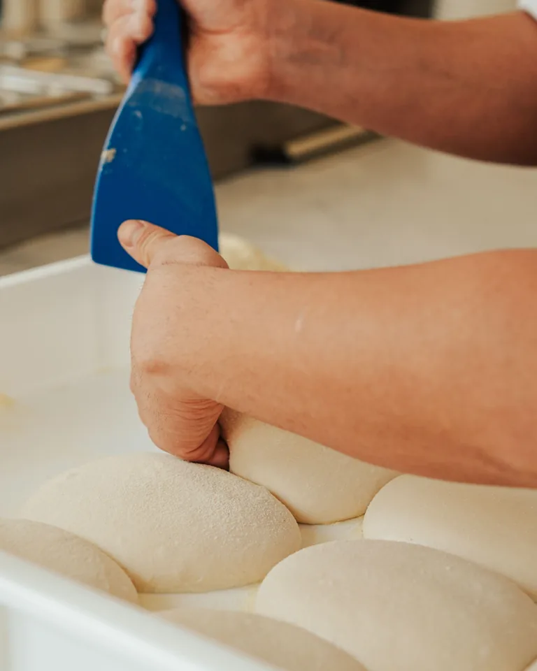A dough scraper gently releasing one proofed dough ball from its tray